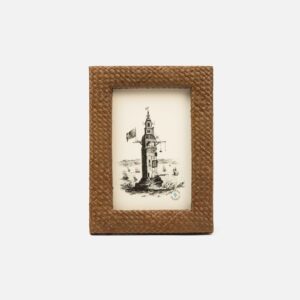 A woven brown picture frame displays a black and white illustration of a lighthouse with ships in the background.