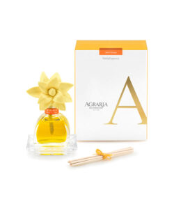 A glass perfume bottle with a yellow flower cap, next to a white box and wooden sticks for fragrance.