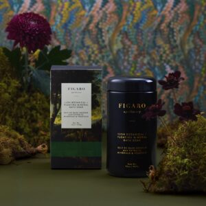 Black container and box of Figaro apothecary bath soak, surrounded by greenery and flowers.