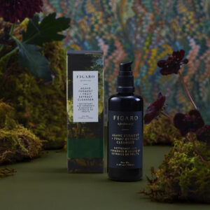 A bottle of Figaro Agave Ferment Cleanser next to its box, surrounded by greenery and flowers.