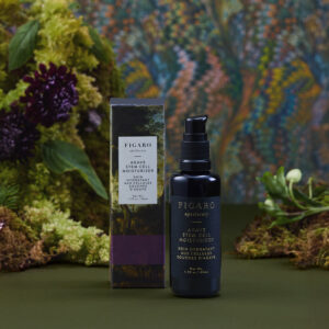 Black bottle of Agave Stem Cell Moisturizer beside its box, surrounded by greenery and a colorful patterned background.