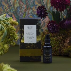 Black bottle of Figaro Active Renewal Face Treatment beside its box, surrounded by greenery and flowers.