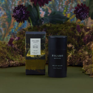 Black cylindrical container of Figaro Relief Balme next to its packaging, set against a colorful floral background.