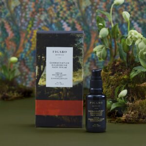 Nourishing face serum bottle next to its box, surrounded by greenery and a colorful background.