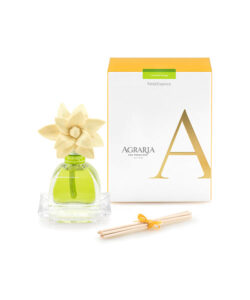 Green glass fragrance bottle with a floral top, next to a yellow box and reed sticks.