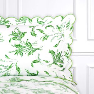 Green and white floral-patterned pillow with scalloped edges on a bed.