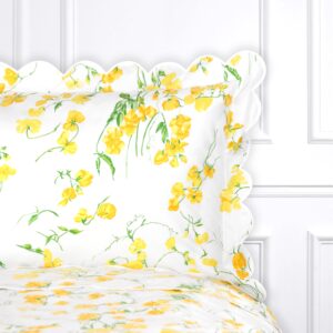 White pillow with yellow floral pattern and scalloped edges, resting on a white bedspread.