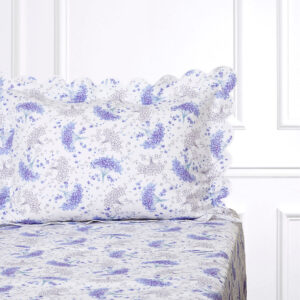 A bed with a floral-patterned pillow and sheet featuring lavender and white designs.