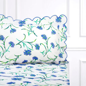 White bedding with blue and green floral patterns, featuring a scalloped pillowcase and matching sheets.