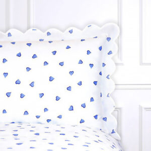 White bedding with blue heart patterns and a scalloped pillow edge.