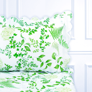 White bedding with green botanical patterns, featuring a scalloped pillow and leafy designs.