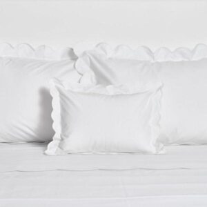 Three white pillows with scalloped edges arranged on a bed.
