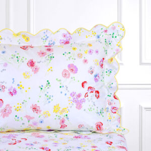 Floral-patterned pillow with scalloped edges on a bed, featuring pink, yellow, and green flowers.
