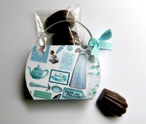 A decorative purse featuring Jane Austen-themed illustrations, with chocolates inside and one chocolate beside it.