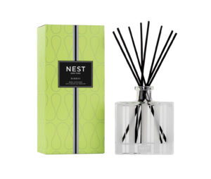 A clear glass reed diffuser with black reeds beside a green box labeled "NEST Bamboo.