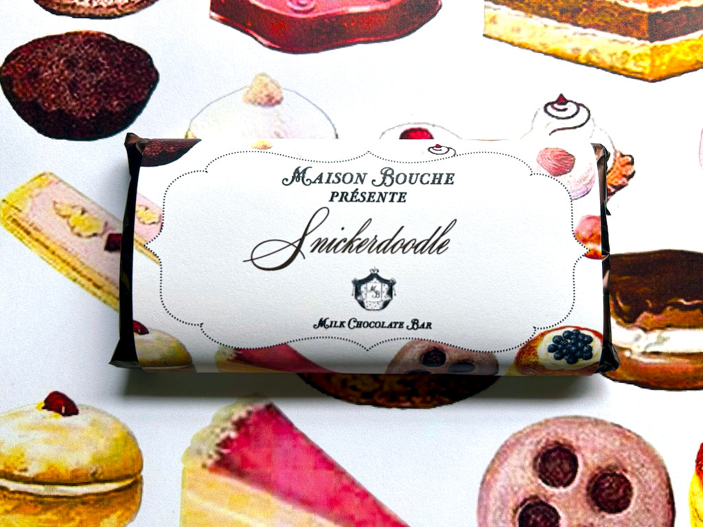 A milk chocolate bar labeled "Snickerdoodle" on a colorful dessert background.