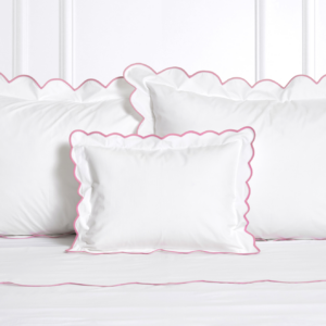 White pillows with pink scalloped edges arranged on a white bedspread.