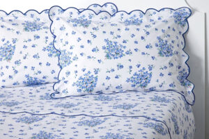 White bedding with blue floral patterns and scalloped edges, featuring two matching pillows.