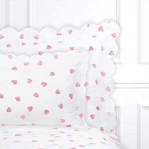 White bedding with pink heart patterns and scalloped edges on pillows.