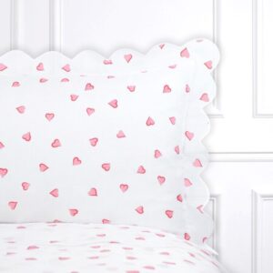 White bedding with scattered pink hearts and scalloped edges on the pillow.