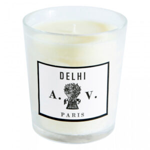 White candle in a clear glass holder with a label reading "Delhi A.V. Paris.
