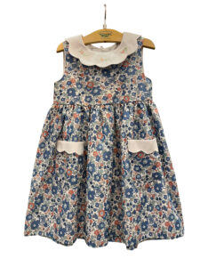 Blue floral dress with a white collar and pockets, hanging on a wooden hanger.