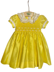 Yellow silk dress with a lace collar and smocked bodice, hanging on a wooden hanger.