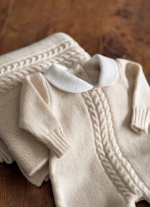 A cream-colored knitted sweater with a white collar, folded beside a matching blanket.