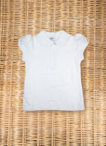 White short-sleeve polo shirt with a ruffled collar, laid flat on a woven surface.
