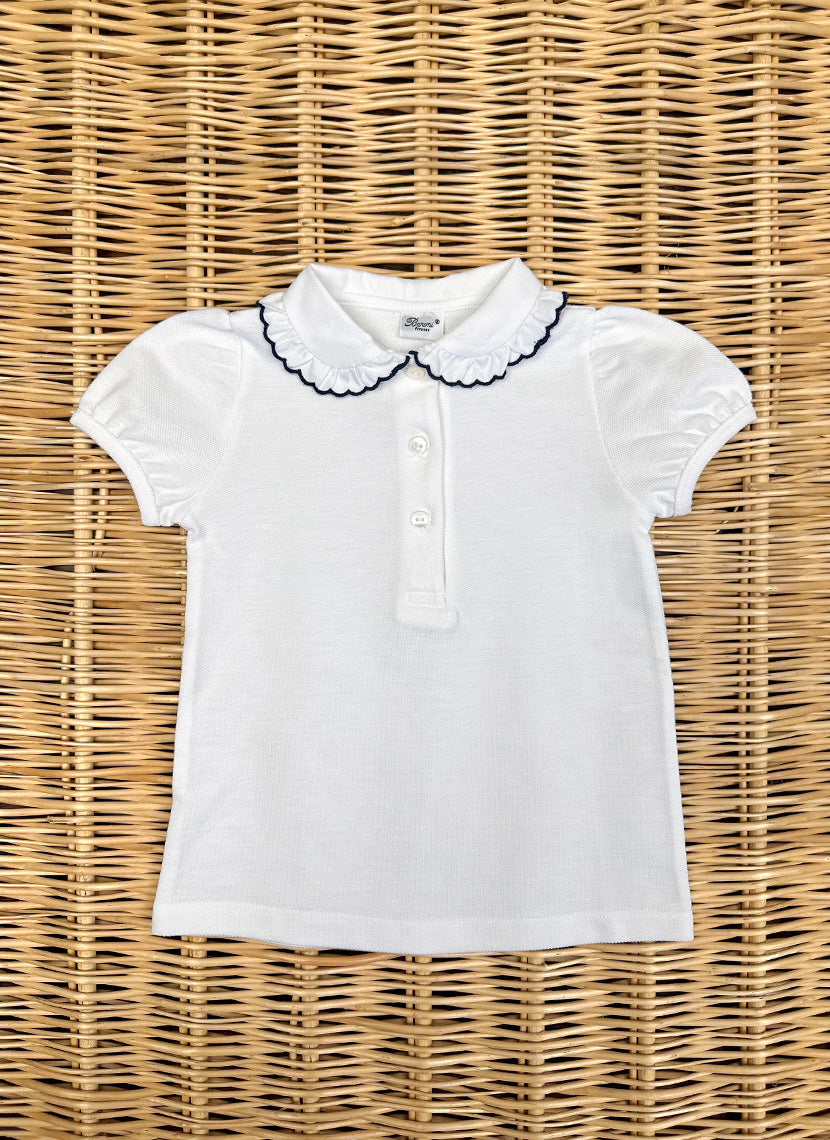 7957blu_1800x1800 White short-sleeve polo shirt with a ruffled collar and three buttons, laid flat on a woven surface.