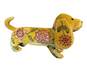 A yellow velvet dachshund with floral embroidery stands on a black background.
