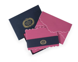 A navy box contains pink stationery with scalloped edges and a decorative band.