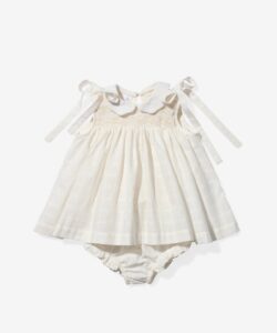 Cream-colored baby dress with a collar, smocked bodice, and ribbon ties, paired with matching bloomers.