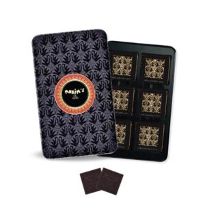 A decorative tin contains twelve dark chocolate squares, with two squares placed outside the tin.