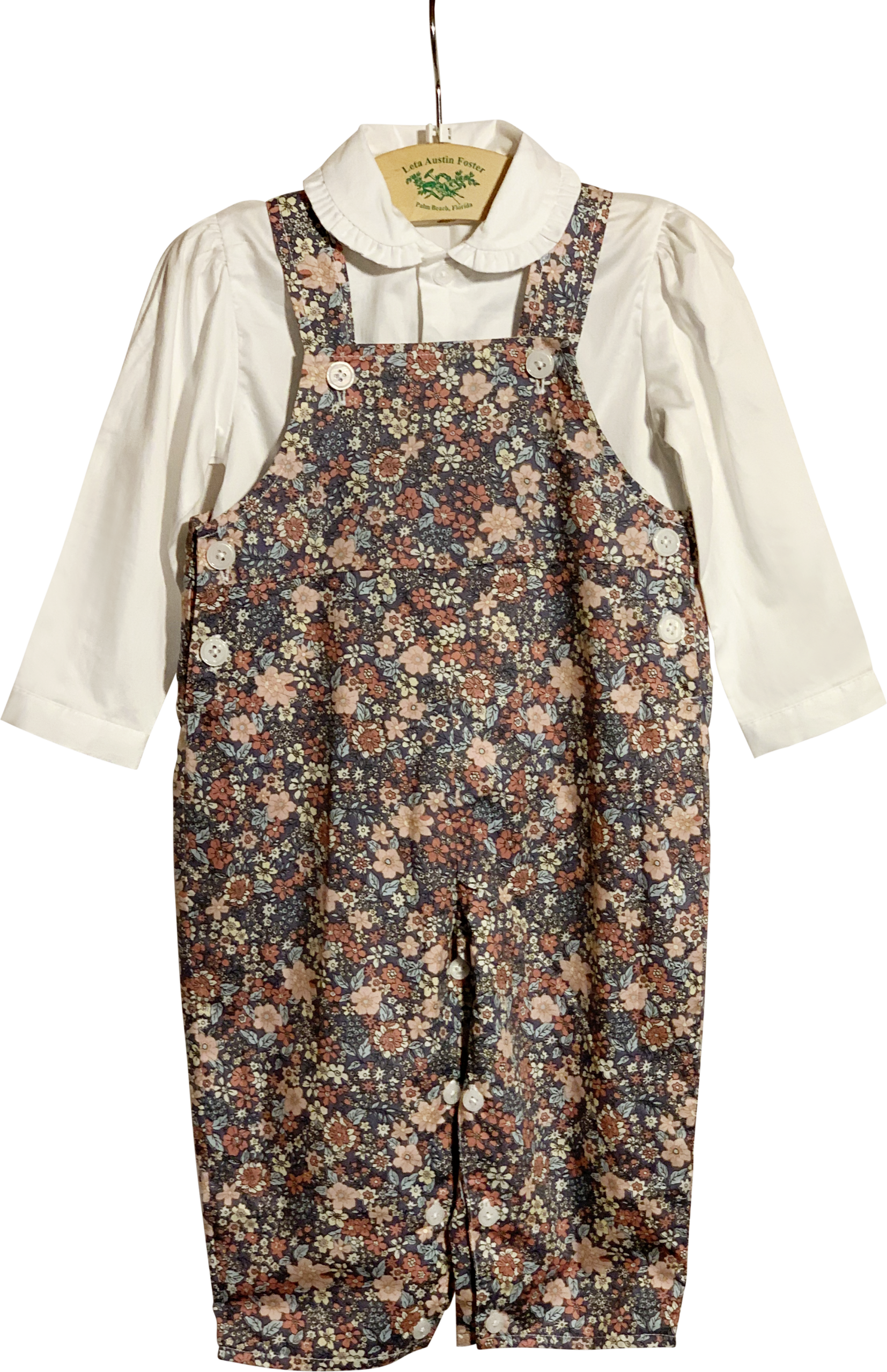 Rachel Riley Pink Floral Overalls Set Floral overalls set with a white collared shirt, hanging on a display.