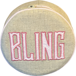 Round jewelry case with "BLING" embroidered in pink on a beige fabric background.