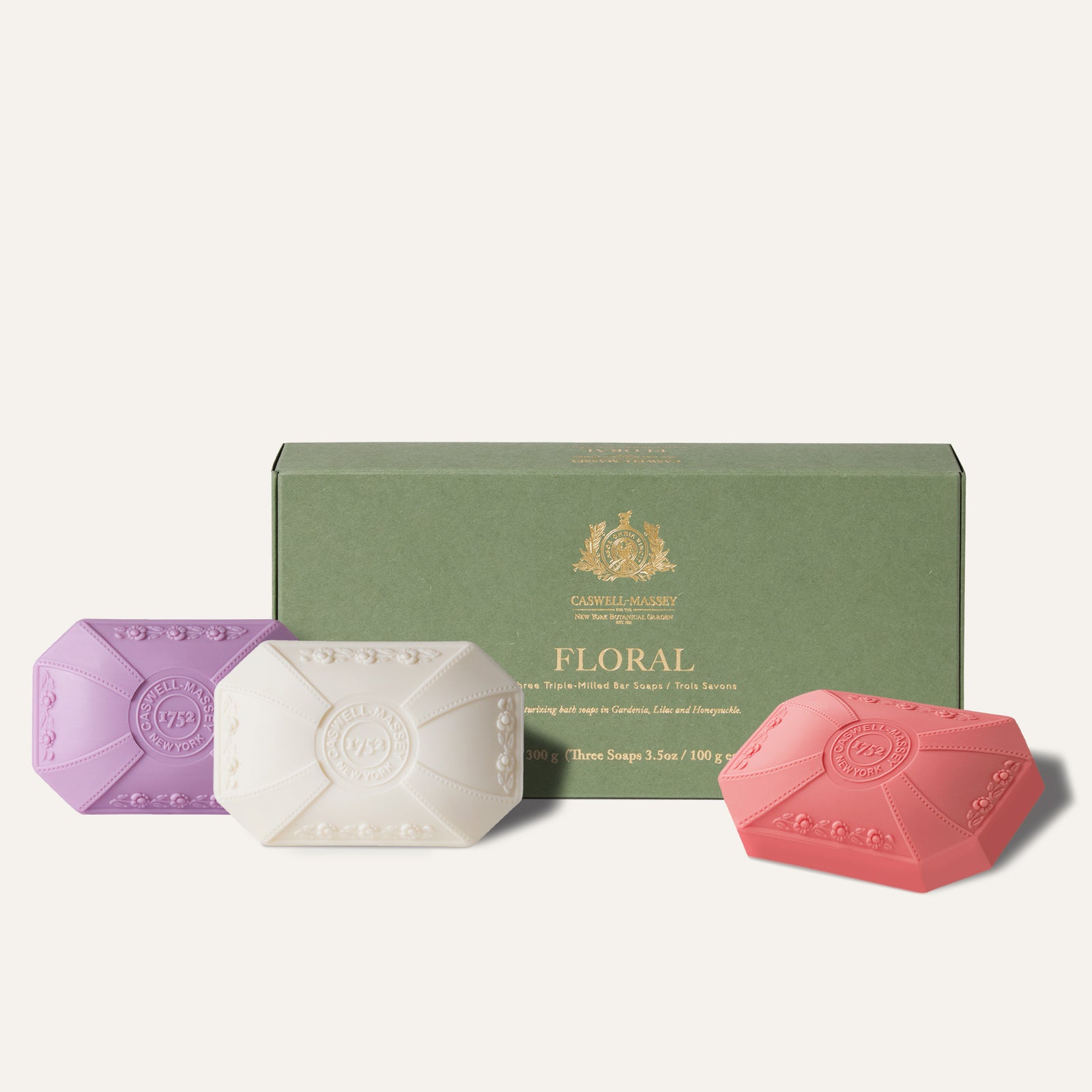 Three floral-scented soaps in purple, white, and pink, displayed in front of a green box.